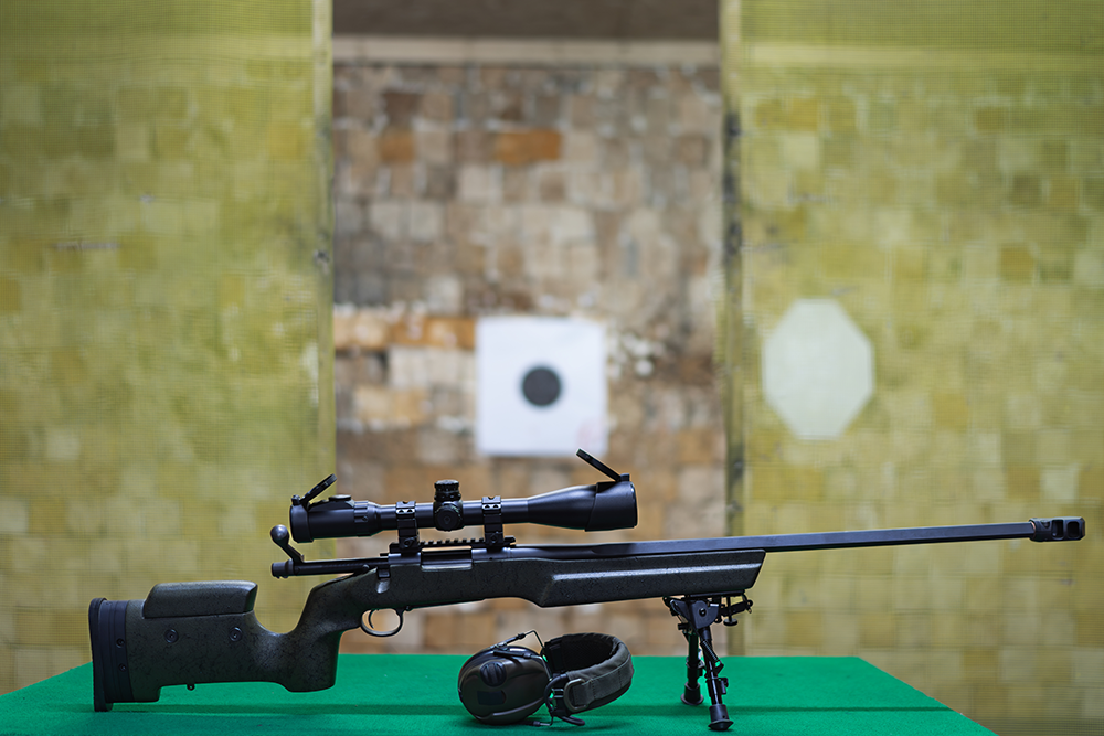 Carabine à verrou avec lunette de tir et bipied en position de repos face à une cible en stand intérieur