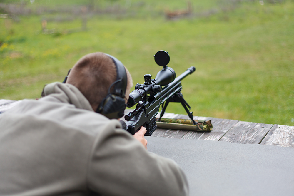 Tireur allongé en position de tir longue distance avec une carabine équipée d'une lunette de tir de précision.