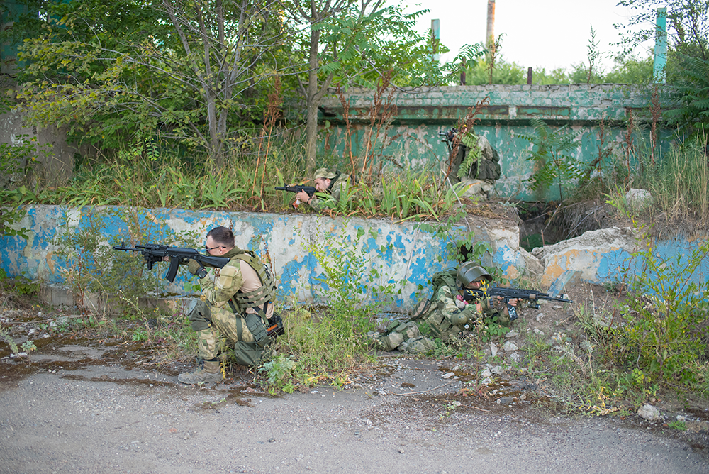 Joueurs d’airsoft en tenue tactique, en position de tir dans un environnement urbain dégradé.
