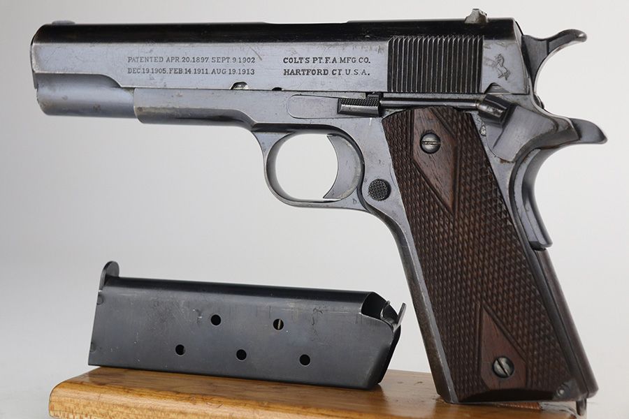 Colt M1911 de 1916 avec chargeur, posé sur un socle en bois, vue latérale.