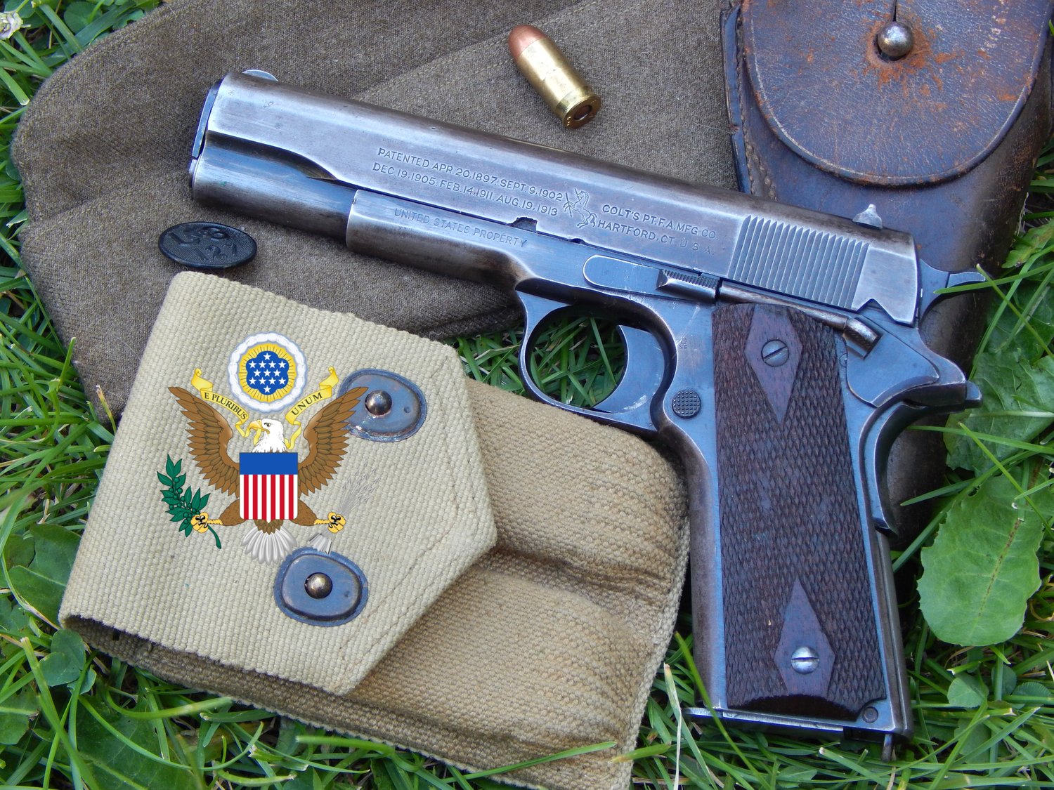 Pistolet M1911 militaire sur de l’herbe, avec son étui, une cartouchière en toile et un emblème des États-Unis.