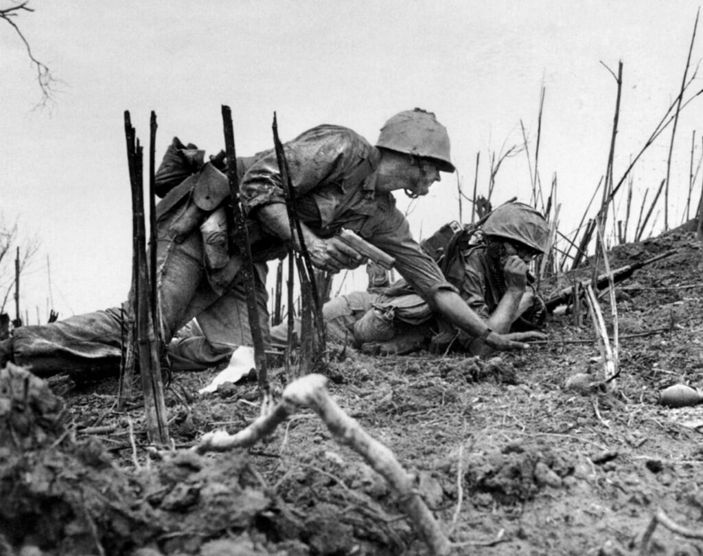 Officier US Marine avec pistolet Colt M1911A1 en main, parlant à un opérateur radio dans la boue au Vietnam, 1967.