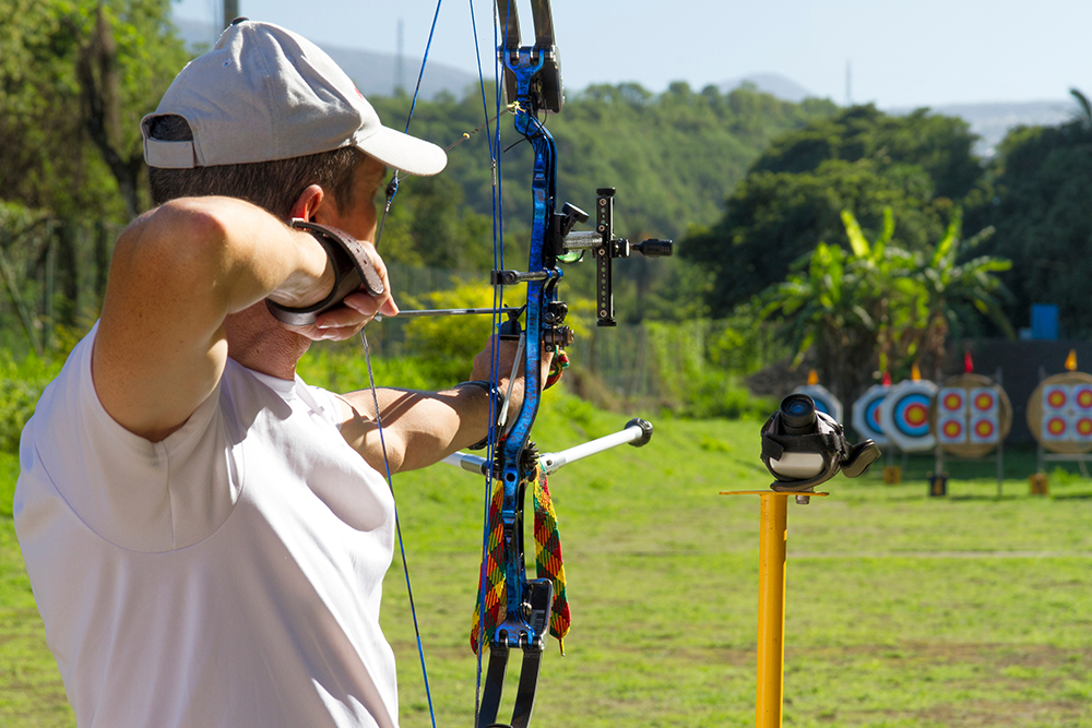 Un archer vise une cible à longue distance avec un arc à poulies équipé, en contexte de compétition extérieure