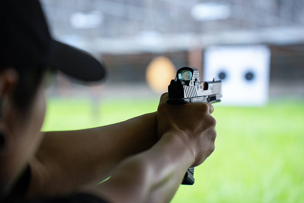 Pratiquant de tir sportif en stand intérieur visant une cible avec un pistolet équipé d’un viseur point rouge