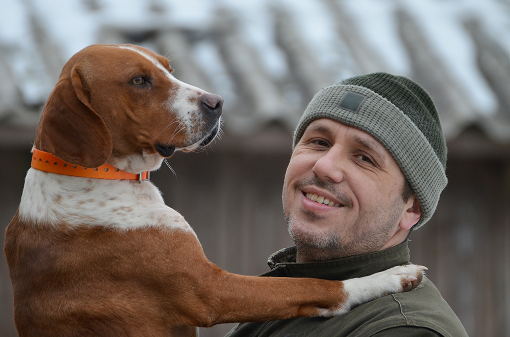 Chien de chasse aux pattes blanches et collier orange câliné par son maître chasseur en bonnet kaki