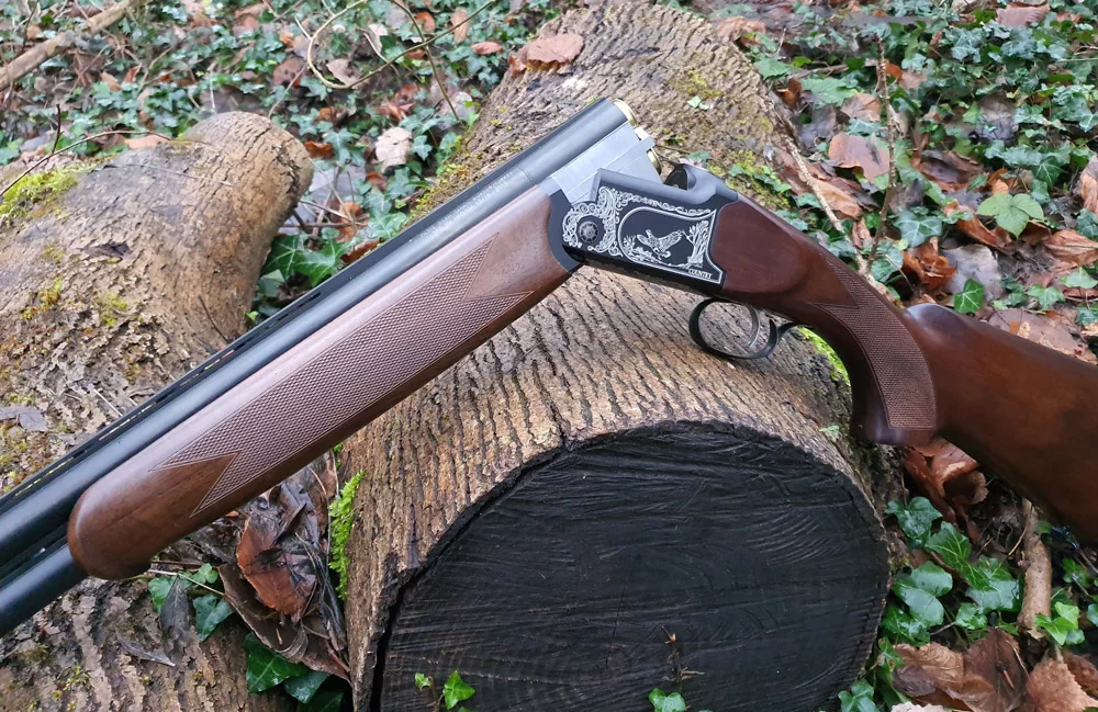 Fusil de chasse superposé Country, avec gravure fine, reposant sur une souche dans un environnement forestier