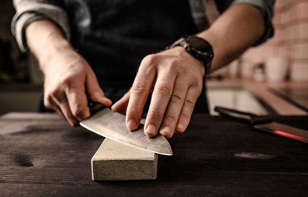 Gros plan sur un affûtage de couteau de cuisine avec une pierre à aiguiser, soulignant la technique rigoureuse.