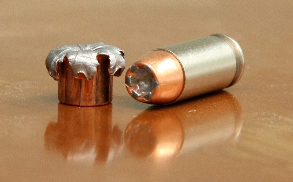 Cartouche Speer Gold Dot de calibre .40 Smith et Wesson de 165 grains, à côté d’une ogive expansée après tir, illustrant la performance balistique du projectile JHP.
