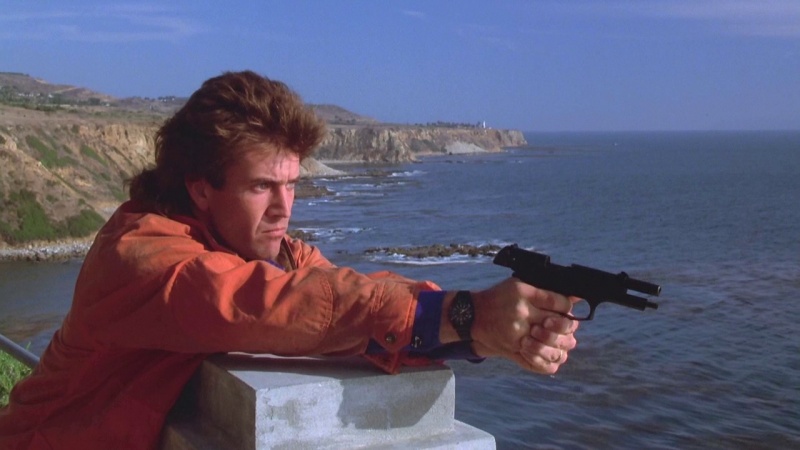 Martin Riggs (Mel Gibson) dans L'Arme Fatale (1987) tenant un Beretta 92F et tirant en direction d’un hélicoptère.

