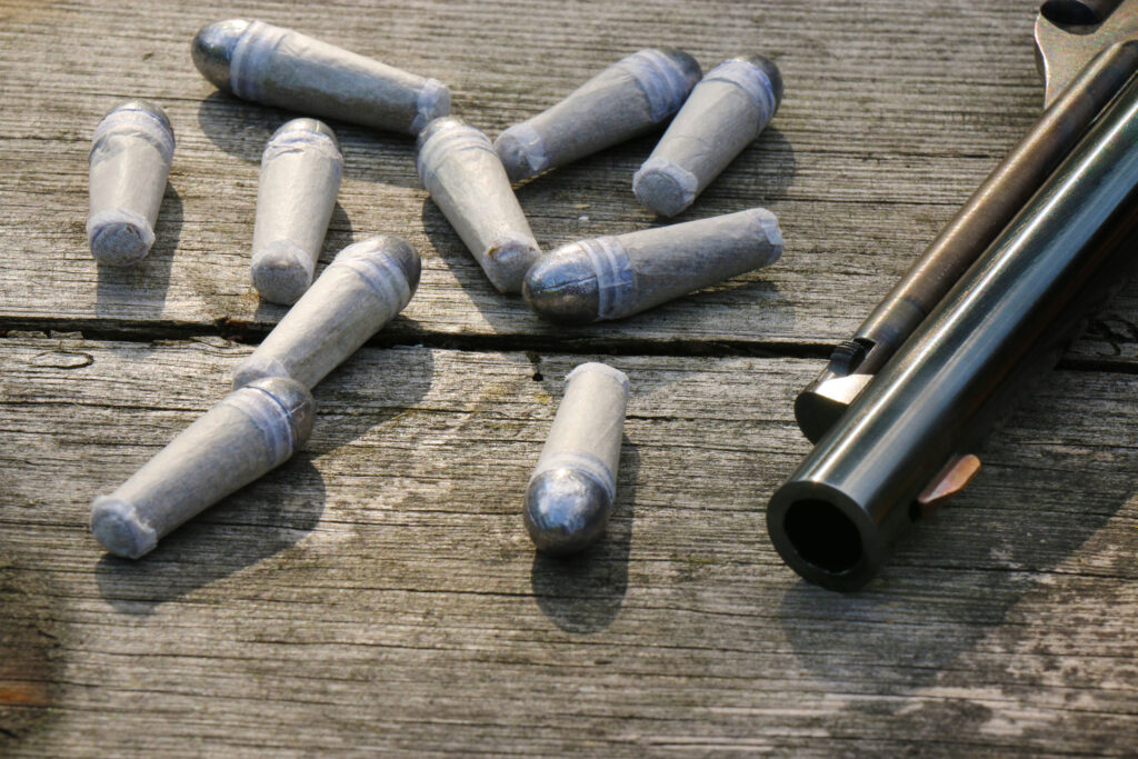 Balles rondes en plomb pour revolver à percussion Remington 1858 posées sur une table en bois.