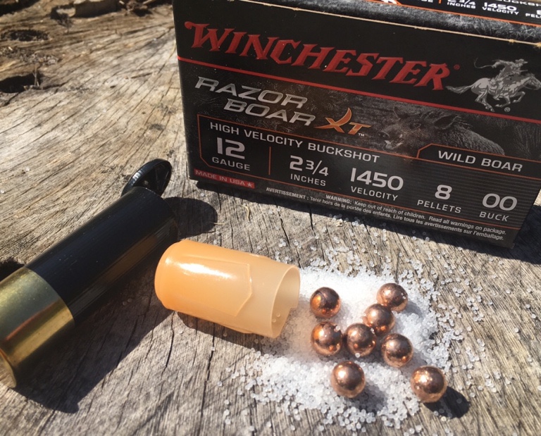 Cartouche Winchester Razor Boar XT ouverte, montrant les projectiles de chevrotine et la poudre, posée sur un support en bois, utilisée pour la chasse au sanglier.