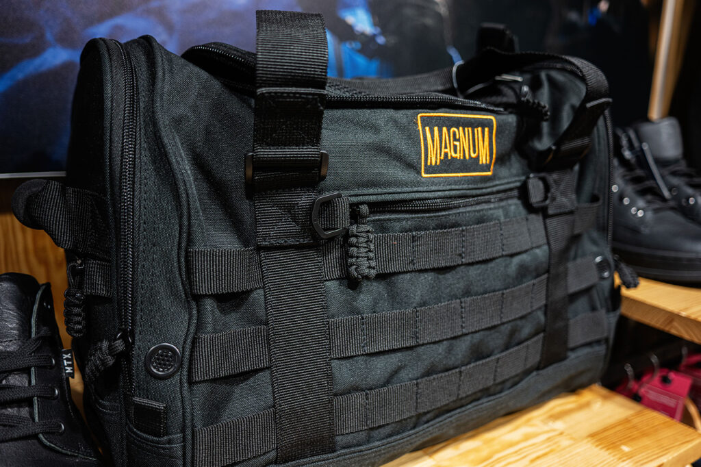 Sac de tir noir avec sangles et logo Magnum posé sur une étagère en bois.