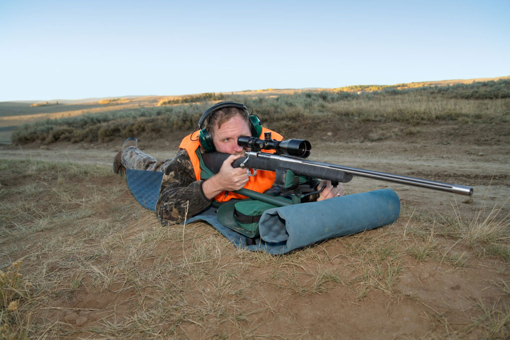 Tireur en position couchée utilisant un tapis de tir avec une carabine équipée d’une lunette de visée.