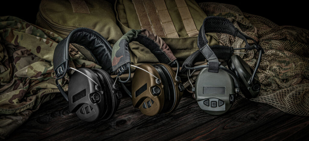 Casques de protection auditive électroniques (actifs) posés sur un sac de tir avec équipement camouflage.