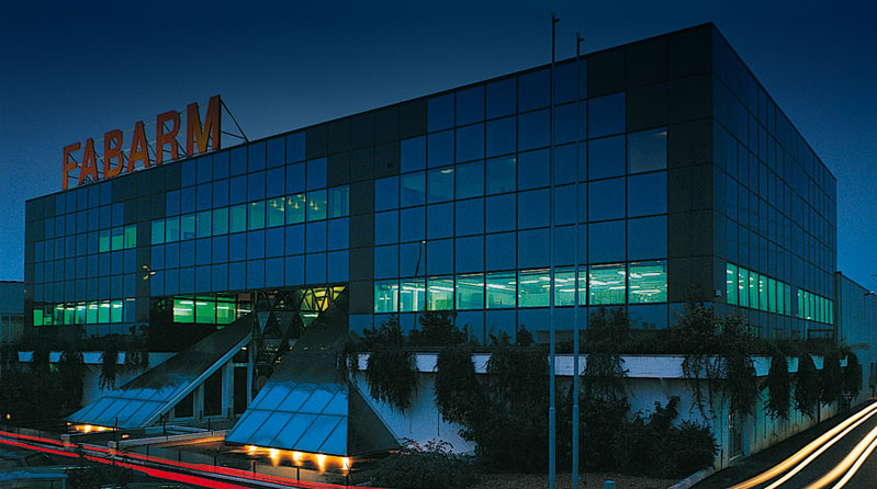 Façade moderne du siège de la société Fabarm à Travagliato, Italie, bâtiment vitré avec le nom FABARM en lettres rouges sur le toit, illustrant les installations industrielles de l’entreprise italienne de fabrication de fusils.