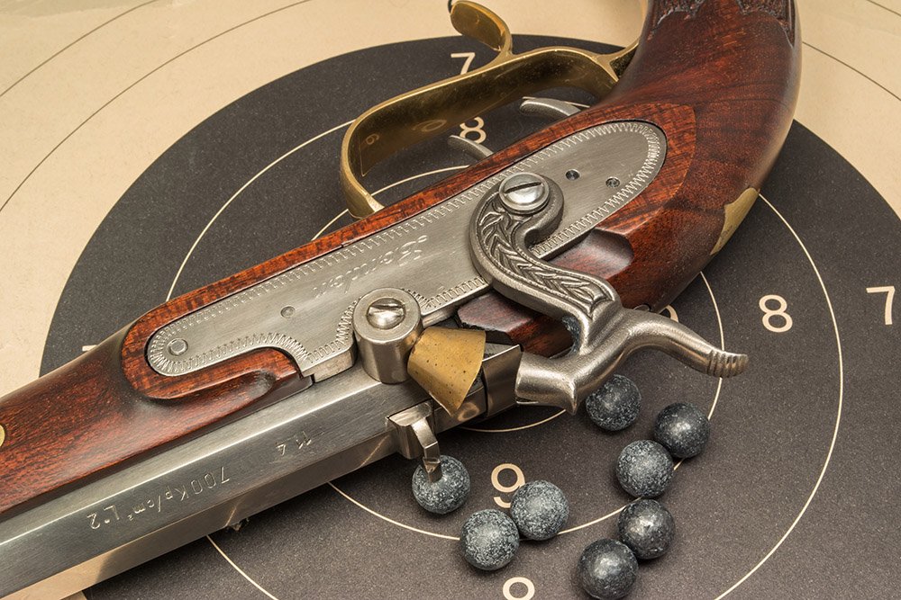 Pistolet à poudre noire traditionnel posé sur une cible de tir avec balles en plomb, illustrant la pratique du tir à la poudre noire pour les débutants.