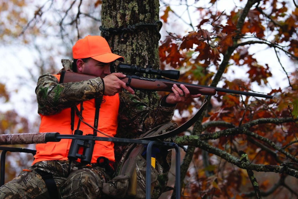 Chasseur posté en forêt avec une carabine à verrou Mossberg Patriot Walnut équipée d’une lunette