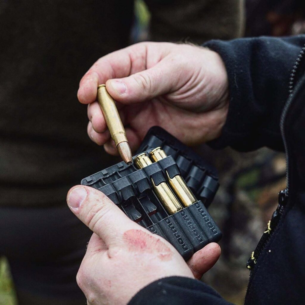 Chasseur tenant une cartouche Norma Vulkan au-dessus d’un porte-cartouches contenant plusieurs munitions de chasse