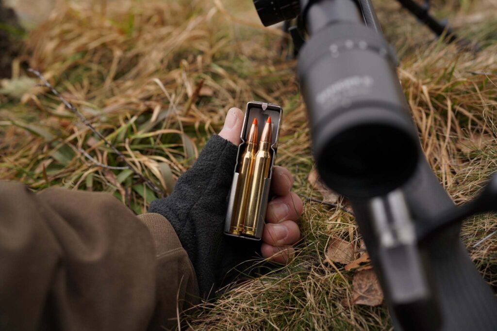Cartouches de chasse Norma Tipstrike à pointe polymère orange dans un chargeur, à côté d’une carabine équipée d’une lunette